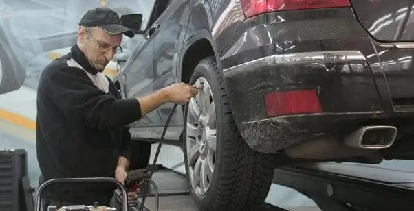 Mehaničar sa kačketom priključuje crevo za vazduh na ventil točka automobila