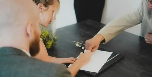 Žena potpisuje dokument dok muškarac pokazuje prstom