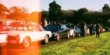 Niz parkiranih automobila i ljudi pored njih na travnatom prostoru sa narandžastom svetlosnom prugom