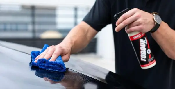 Osoba briše krov automobila plavom mikrovlaknom dok drži sprej